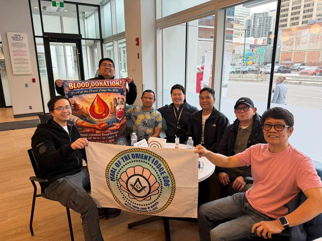 Members of Pearl of the Orient Lodge No. 206 at a blood donation event, holding the lodge flag and a blood donation banner.